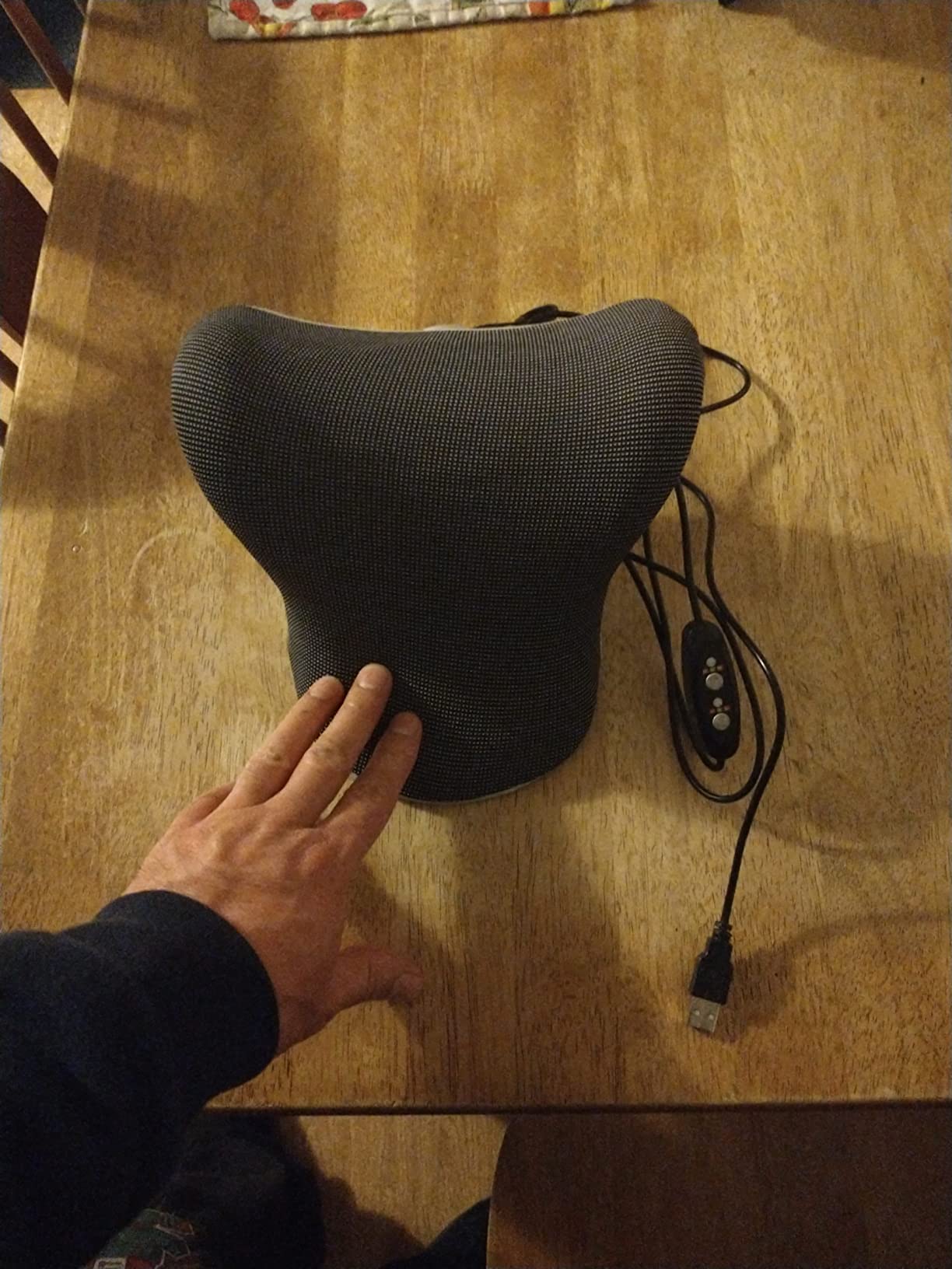 A person on a chair with a black cushion, showcasing the Neck and Shoulder Relaxer Pillow in use for a product review.