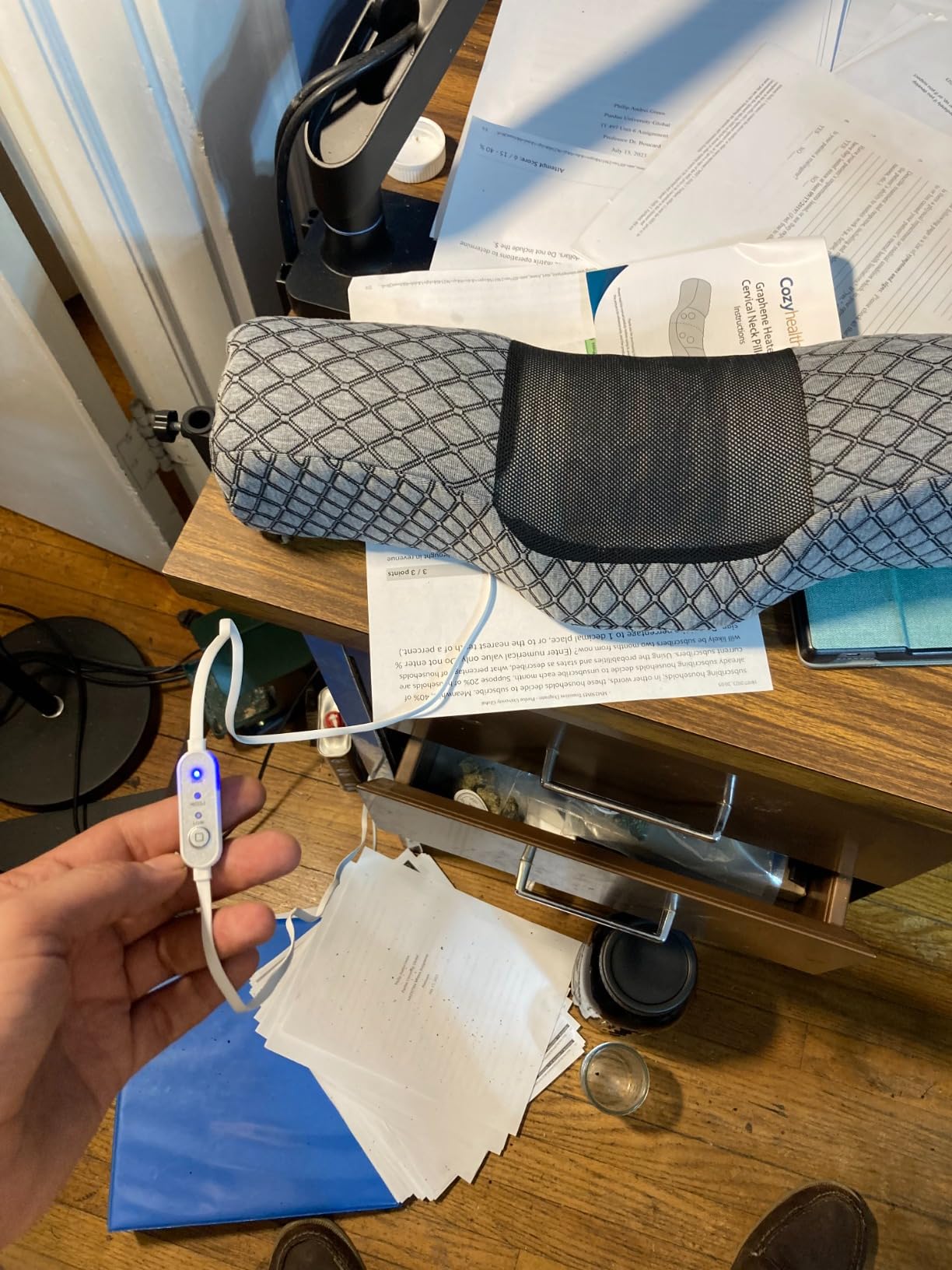 A person holds a remote control beside a computer while using Roll Pillows for Neck Pain Relief for comfort during work.