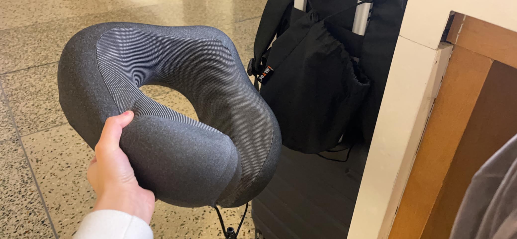 A person holds a gray MLVOC Travel Pillow in front of a suitcase, showcasing it in use for a product review.